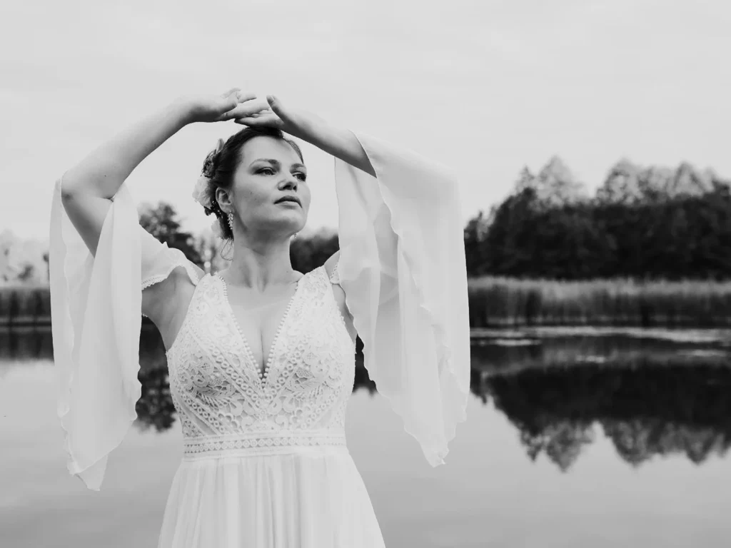 Brud poserer med ynde foran en sø i en elegant kjole, fotograferet i sort-hvid af bryllupsfotograf på Sjælland nær København.