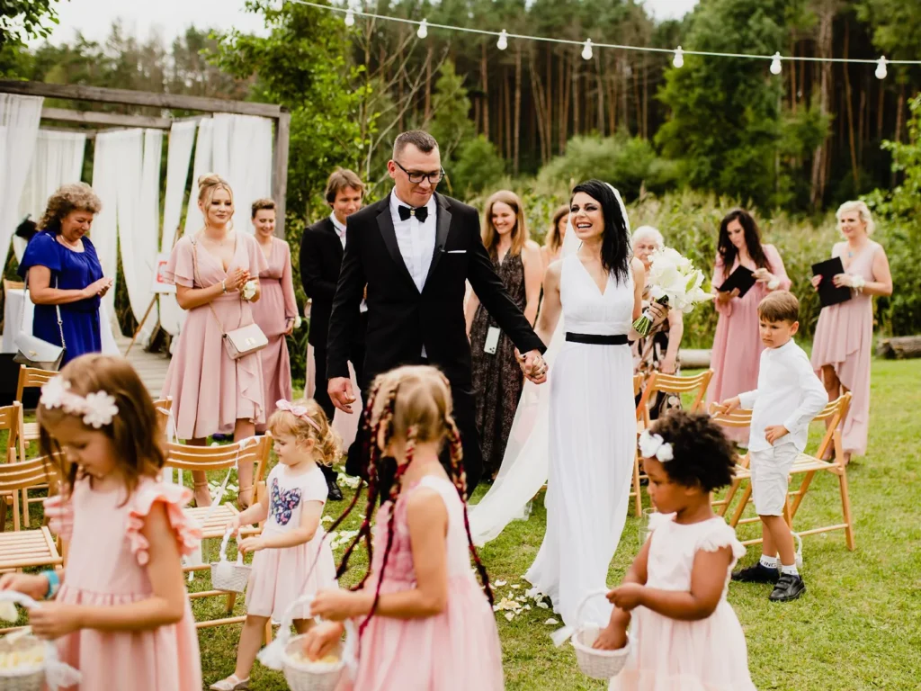 Brudeparret forlader ceremonien hånd i hånd omgivet af glade gæster og blomsterbørn, fotograferet af bryllupsfotograf på Sjælland nær København.