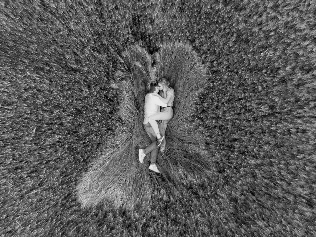 Romantisk par liggende i en hvedemark, fotograferet ovenfra i sort-hvid, taget af bryllupsfotograf på Sjælland nær København.