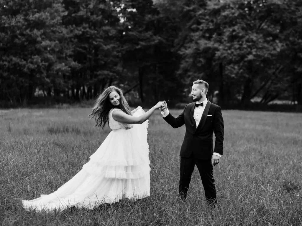 Brudepar danser i en åben eng med træer i baggrunden, fanget i sort-hvid af en bryllupsfotograf på Sjælland nær København.