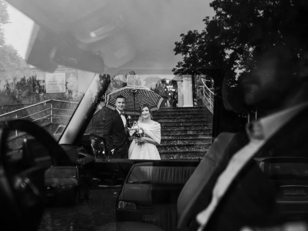 Brudepar fotograferet i regnvejr under en paraply, reflekteret gennem bilruden, taget af bryllupsfotograf på Sjælland nær København.