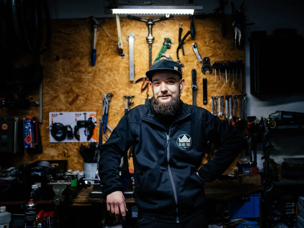 Portræt af en cykelmekaniker foran et vægfyldt værksted med værktøj.