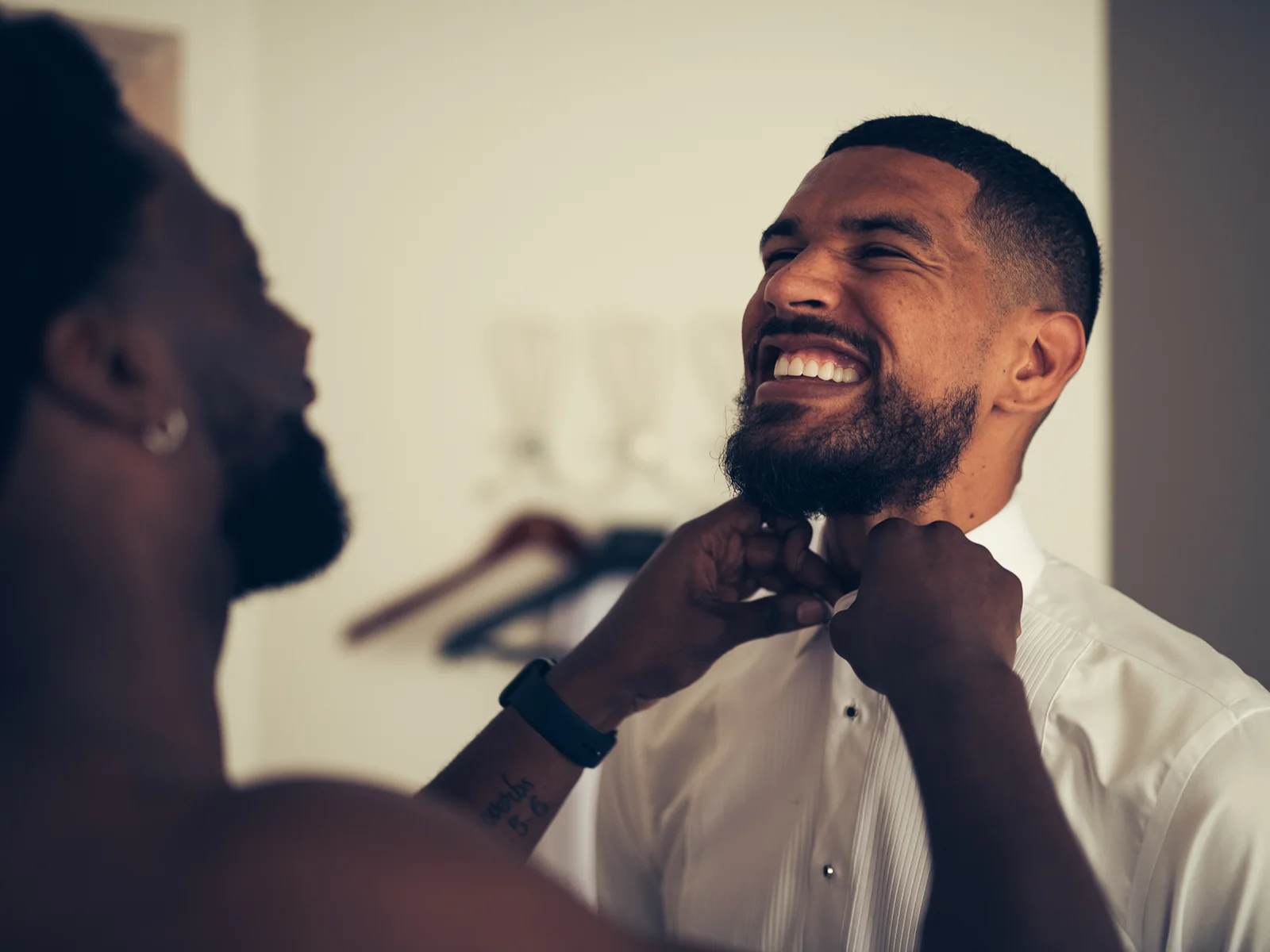 Brudgom smiler bredt, mens en ven hjælper ham med at rette hans butterfly – intime og sjove bryllupsbilleder fra en bryllupsfotograf i København og på Sjælland.