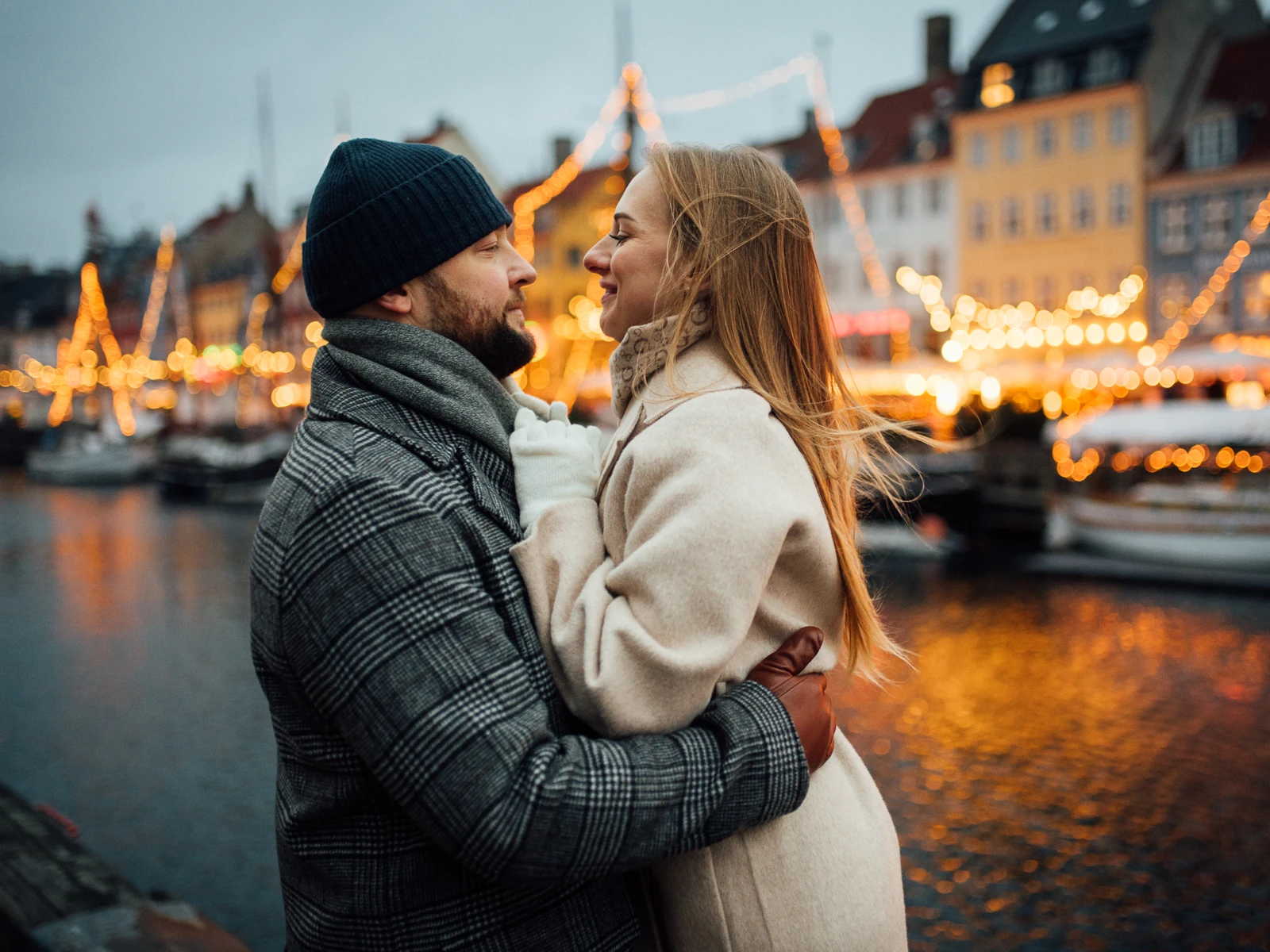 Foreviget kærlighed i hjertet af Nyhavn – Parfotografering med lys og stemning Et smukt par deler en romantisk stund foran de festlige julelys i Nyhavn, København.