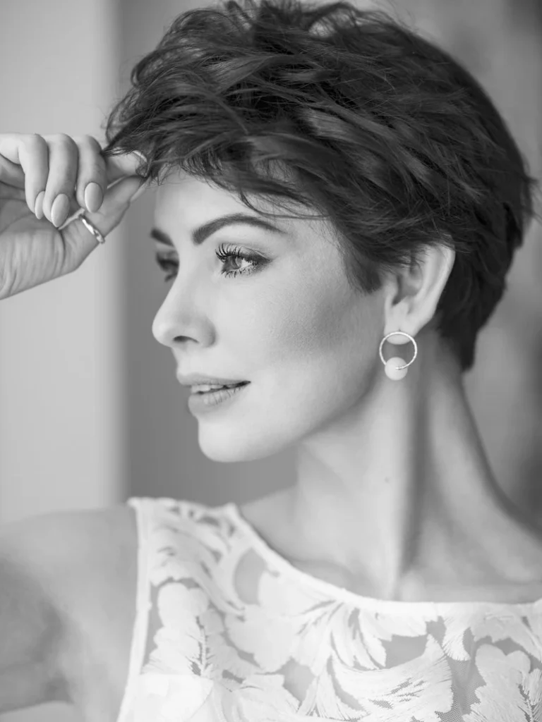 Sort-hvid portræt af en kvinde med kort hår, elegant makeup og smukke ørestikker, iført en blomstermønstret top.