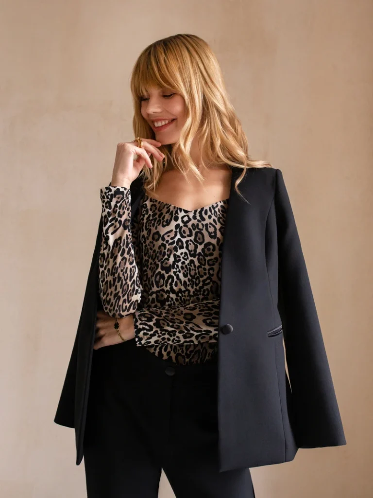 Elegant kvinde i leopardprintet bluse og sort blazer, der smilende ser væk, perfekt modeportræt.